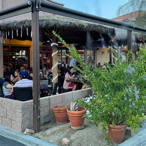 Guillermo's Restaurante patio with people dining under a thatched roof and misters, surrounded by potted plants.