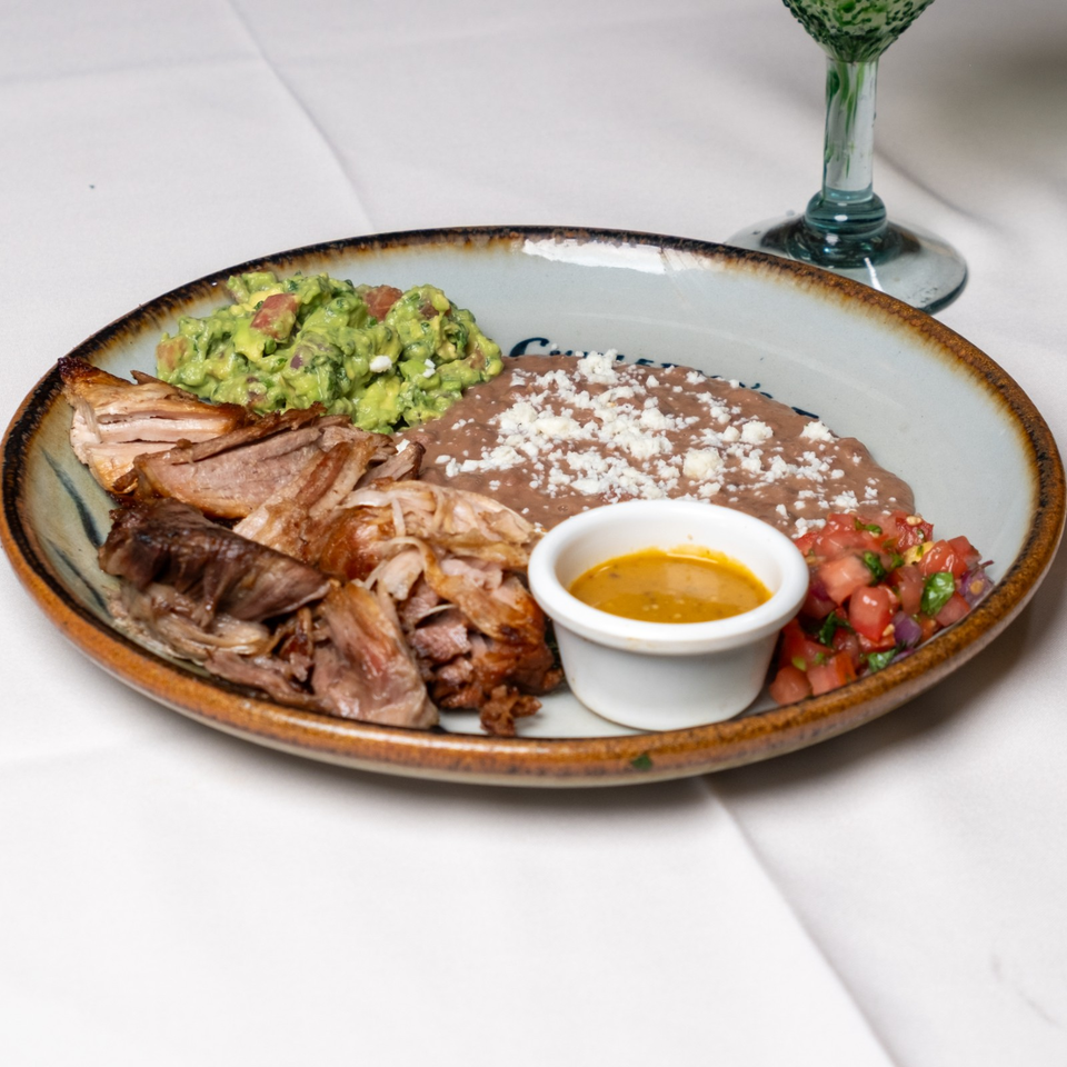 Mexican platter with shredded roasted meat, refried beans topped with cheese, guacamole, pico de gallo, and dipping sauce.