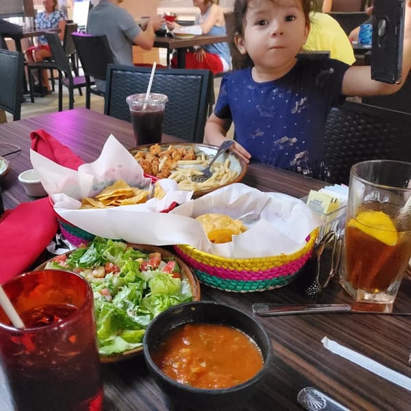 A child sits at a table with a spread of Mexican food, including chips, salsa, and salad.