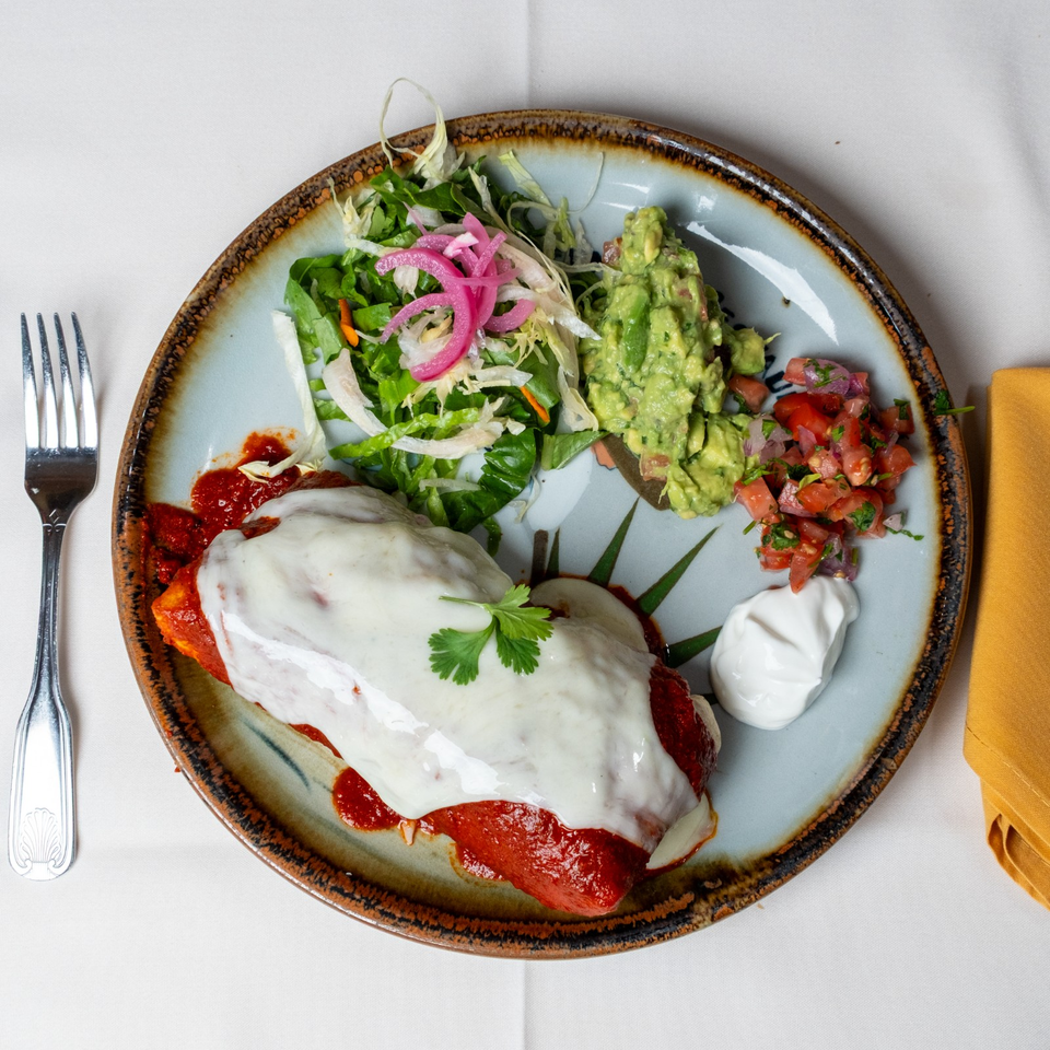 Mexican-style enchiladas topped with melted cheese, served with salad, guacamole, pico de gallo, sour cream, and salsa.