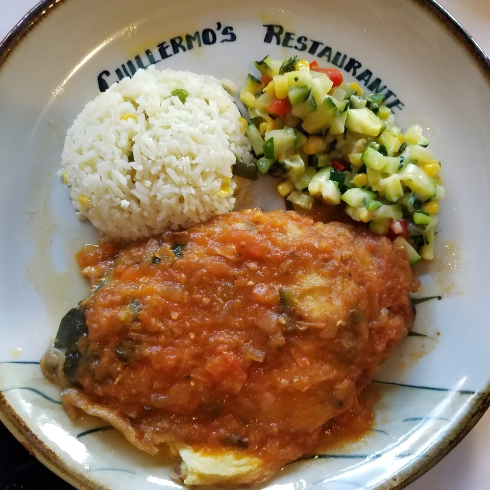 A Mexican dish with a chile relleno covered in red sauce, white rice, and a side of diced vegetables.