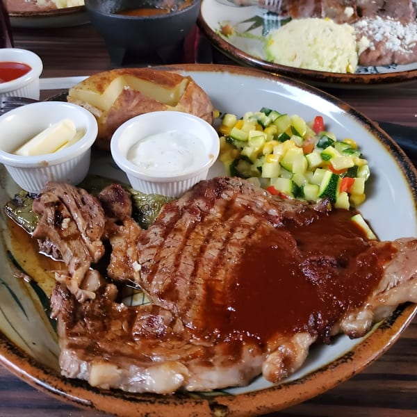 Guillermo's Restaurante's steak with sauce, baked potato, and mixed vegetables on a rustic plate.