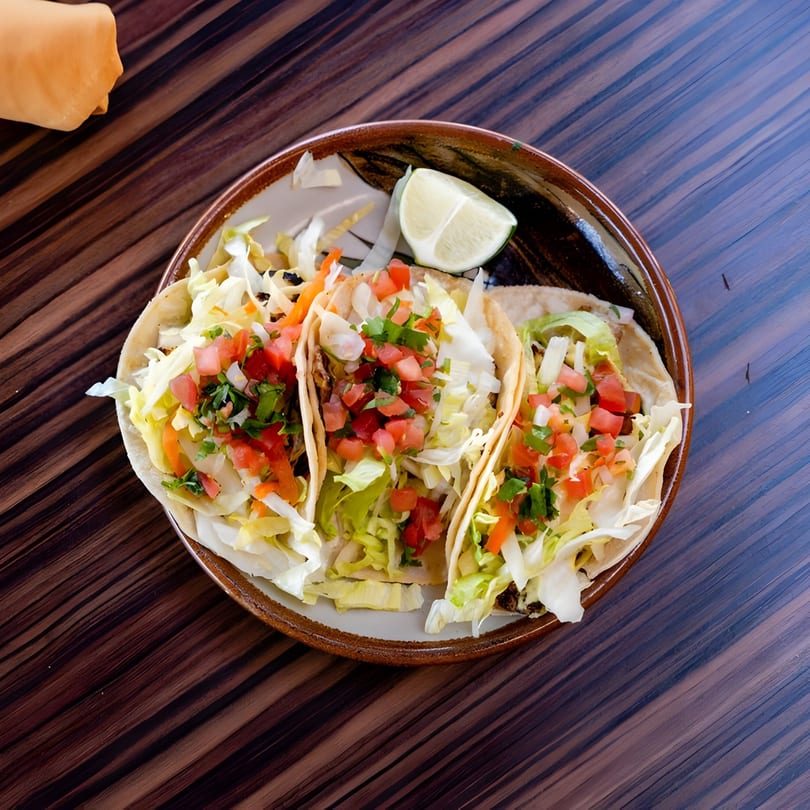 Three Guillermo's Restaurante tacos with shredded lettuce, pico de gallo, and a lime wedge.