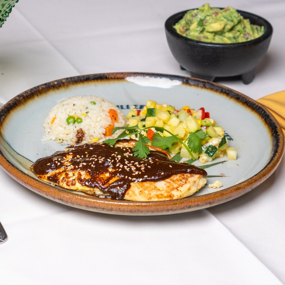 Grilled chicken topped with dark sesame sauce, served with vegetable rice, corn salad, cilantro, and guacamole.