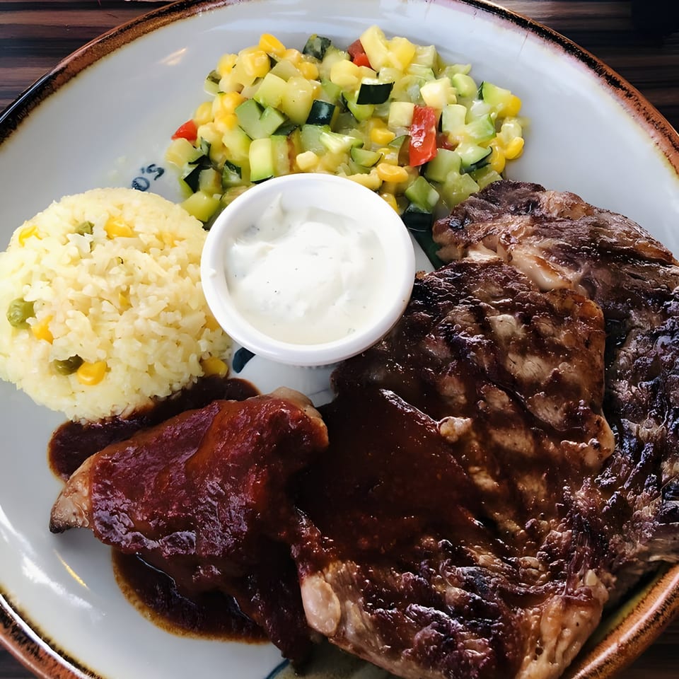 Guillermo's Mexican steak with rice, vegetable medley, and sour cream on a white plate.