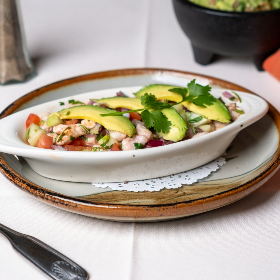 Seafood ceviche topped with avocado slices and cilantro, served in a white dish on a rustic plate.