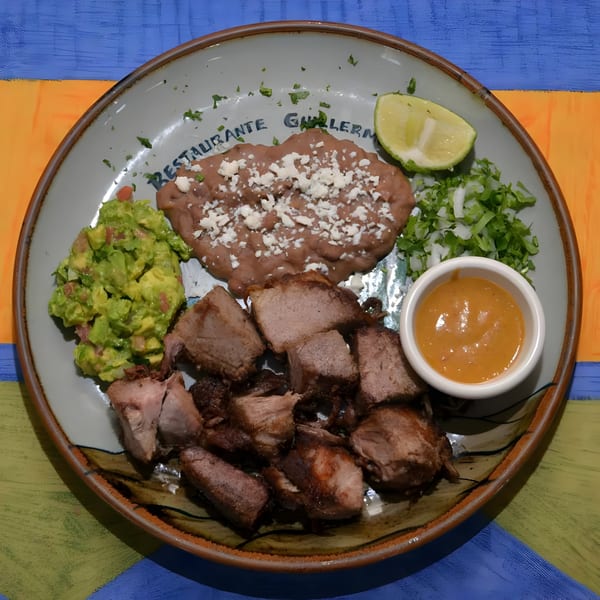 Guillermo's carnitas plate with refried beans, guacamole, chopped onions, cilantro, and sauce.