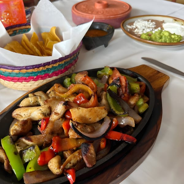 Sizzling chicken fajitas with colorful peppers and onions, served with chips, salsa, beans, and guacamole.